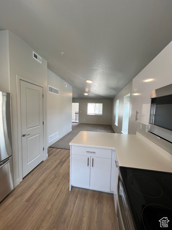 Kitchen with appliances with stainless steel finishes, a peninsula, light wood finished floors, light countertops, and lofted ceiling