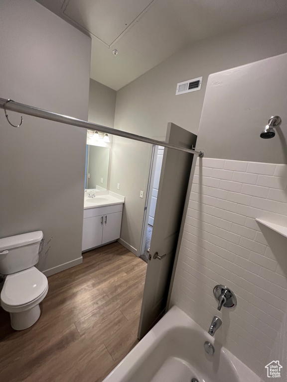 Full bath with wood finished floors, vaulted ceiling, toilet, washtub / shower combination, and vanity