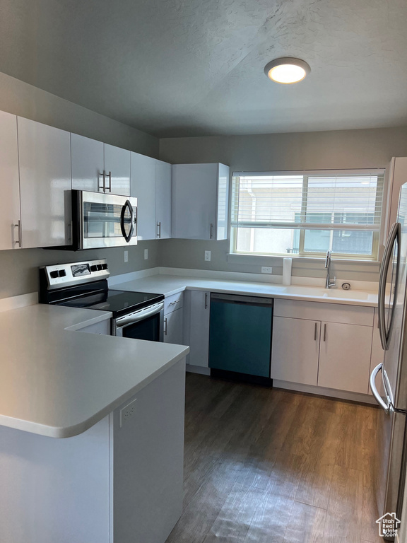 Kitchen with appliances with stainless steel finishes, dark wood-style flooring, a peninsula, light countertops, and white cabinets