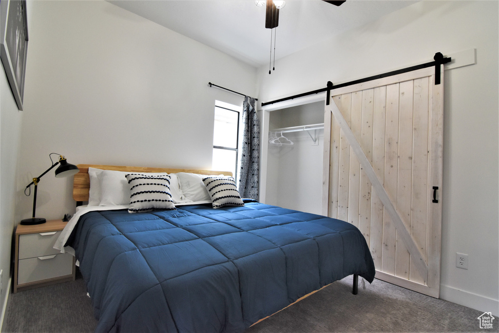 Carpeted bedroom featuring a barn door, a closet, a ceiling fan, and baseboards