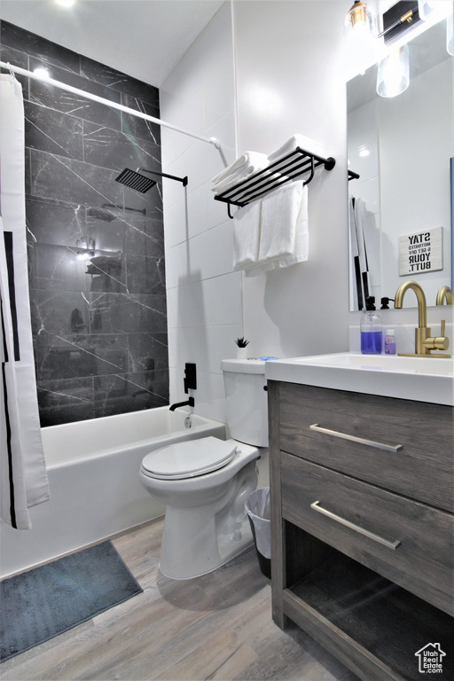 Bathroom with wood finished floors, shower / bath combo with shower curtain, vanity, and toilet