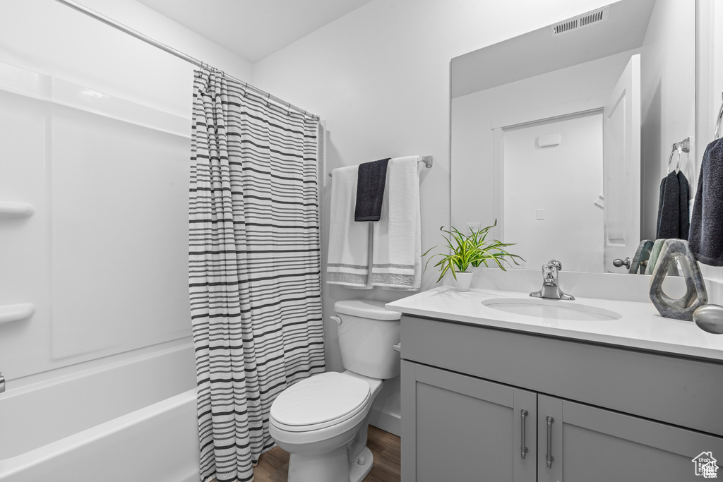 Bathroom with toilet, vanity, wood finished floors, and shower / tub combo with curtain