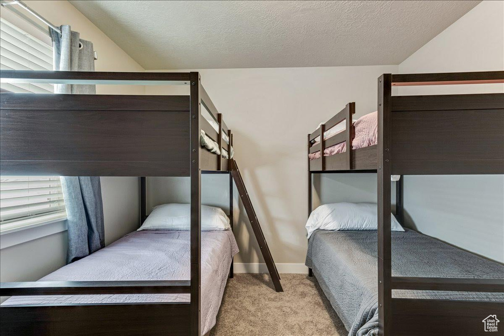 Carpeted bedroom featuring baseboards, lofted ceiling, and a textured ceiling