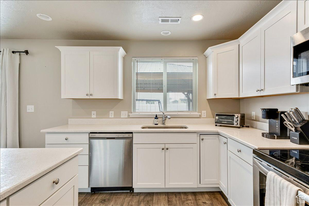 Kitchen featuring appliances with stainless steel finishes, white cabinets, a sink, wood finished floors, and light countertops