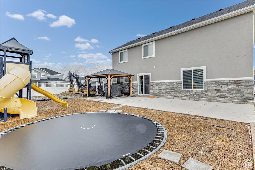 Rear view of house featuring a gazebo, a trampoline, a patio, stone siding, and stucco siding