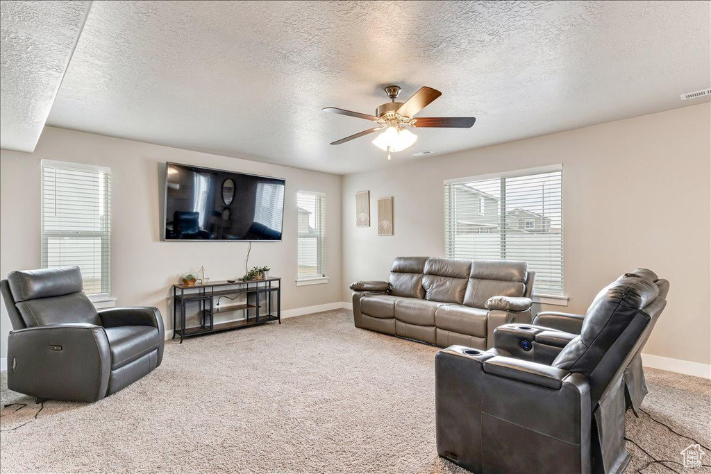 Carpeted living area with ceiling fan, a textured ceiling, and baseboards