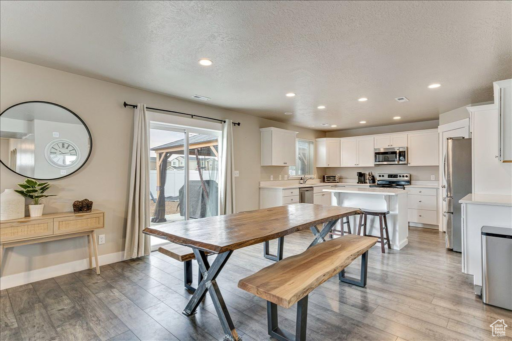 Dining room featuring light wood finished floors, a textured ceiling, recessed lighting, and baseboards