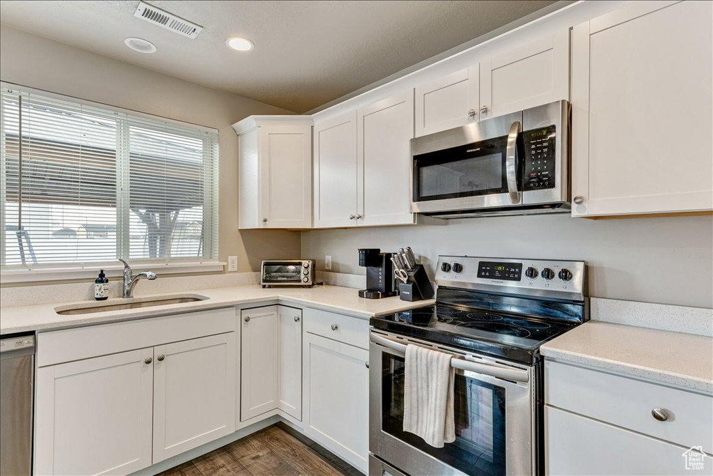 Kitchen with stainless steel appliances, a sink, wood finished floors, white cabinets, and light countertops
