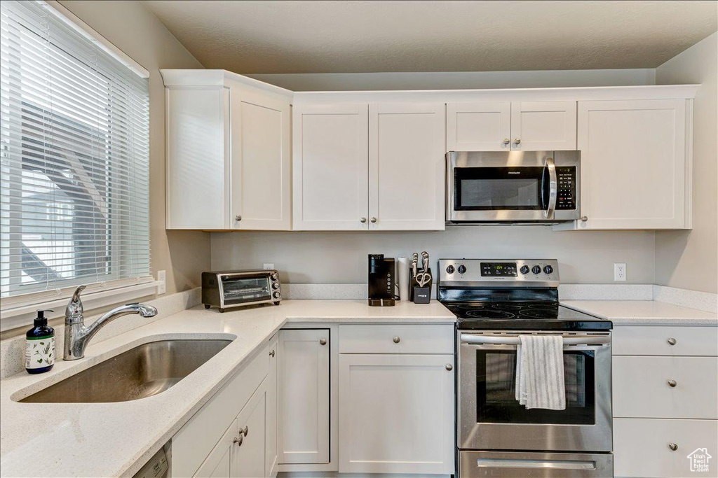 Kitchen with appliances with stainless steel finishes, a sink, and white cabinets