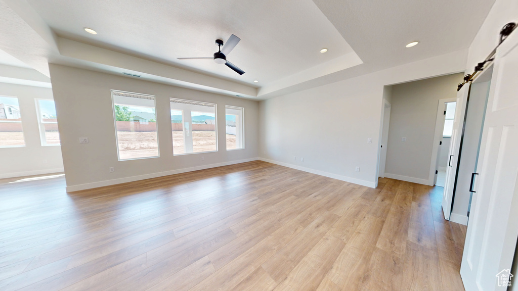 Unfurnished room with a tray ceiling, a barn door, light wood-style floors, a ceiling fan, and recessed lighting