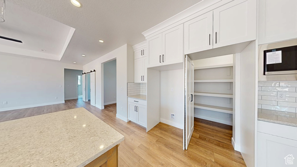 Kitchen with built in microwave, decorative backsplash, light wood finished floors, light stone countertops, and recessed lighting