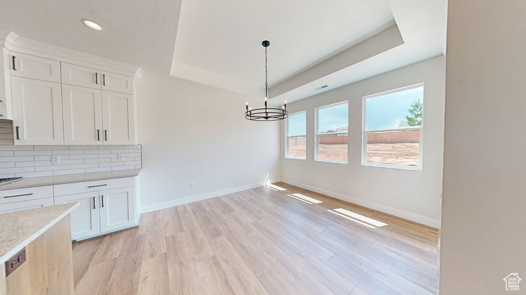 Unfurnished dining area with a tray ceiling, light wood-style flooring, baseboards, a chandelier, and recessed lighting