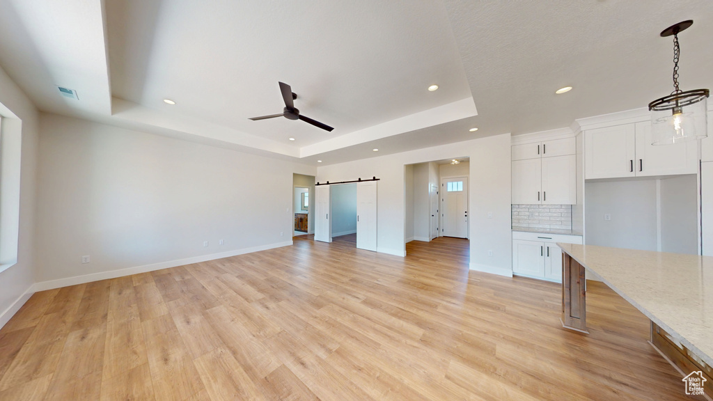 Unfurnished living room featuring a barn door, a raised ceiling, recessed lighting, ceiling fan, and light wood finished floors