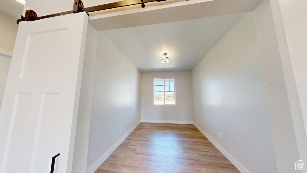 Unfurnished room with light wood finished floors, baseboards, and a barn door