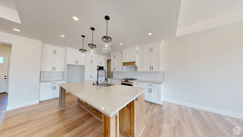 Kitchen with stainless steel range with gas stovetop, a sink, recessed lighting, a spacious island, and light wood finished floors