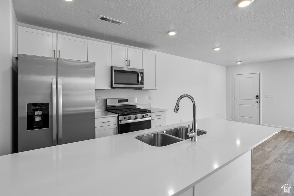 Kitchen featuring stainless steel appliances, a sink, light wood-type flooring, white cabinets, and recessed lighting