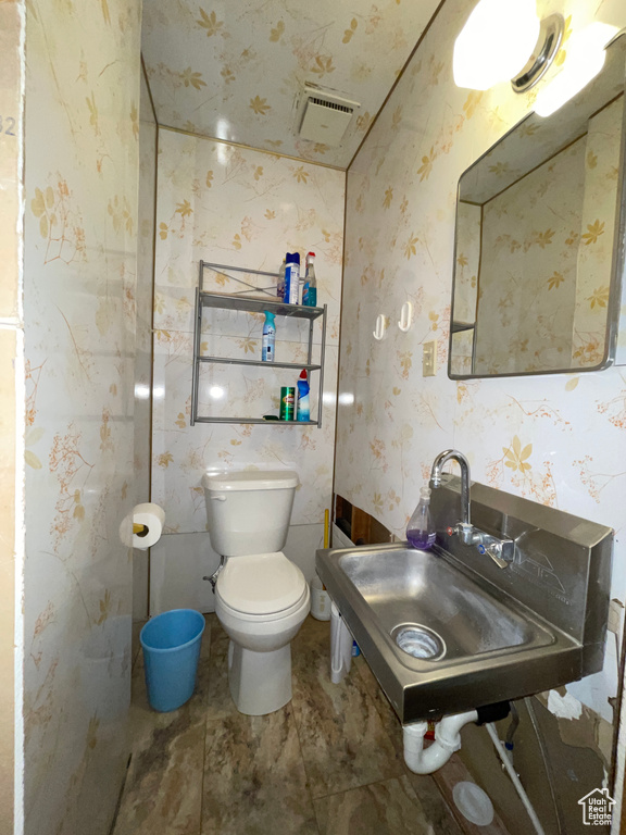 Half bath featuring toilet, wallpapered walls, and a sink