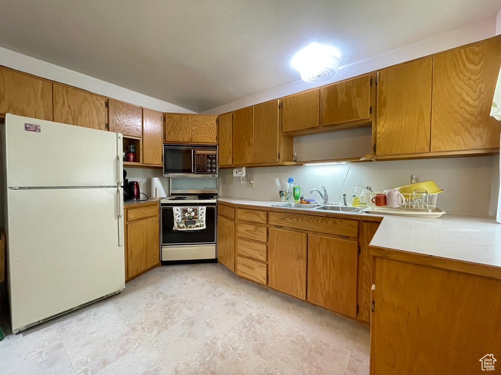 Kitchen featuring white appliances, a sink, light countertops, brown cabinetry, and lofted ceiling