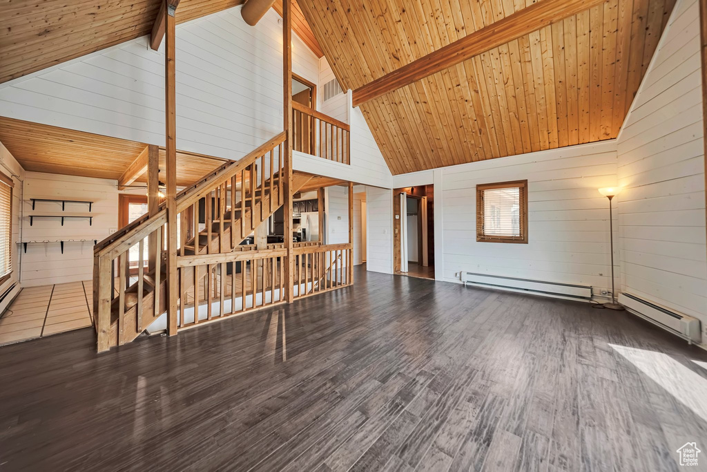 Unfurnished living room with wooden walls, a baseboard radiator, high vaulted ceiling, wood finished floors, and stairs