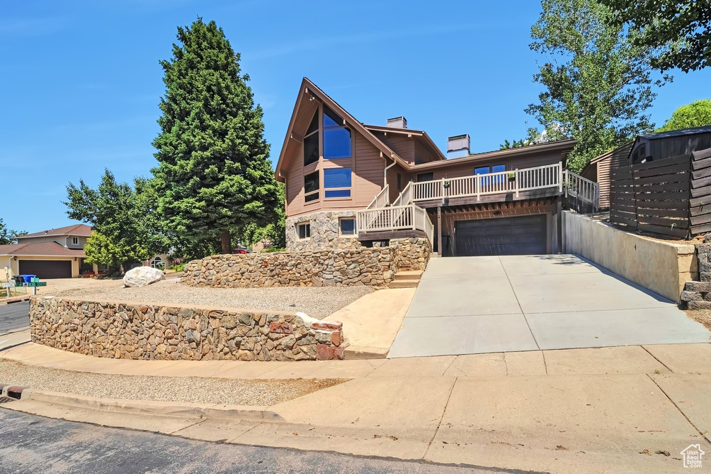 View of front facade with a chimney, stone siding, an attached garage, and concrete driveway