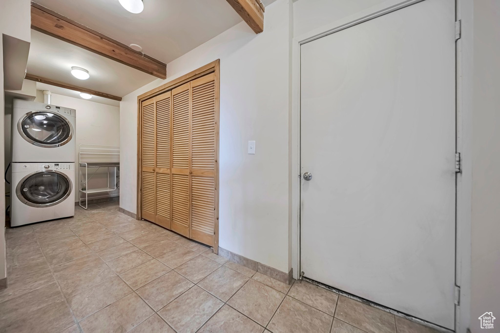Washroom with estacked washer and dryer, light tile patterned floors, and baseboards