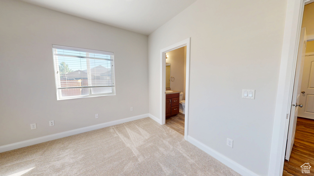 Unfurnished bedroom featuring baseboards, light carpet, and ensuite bathroom