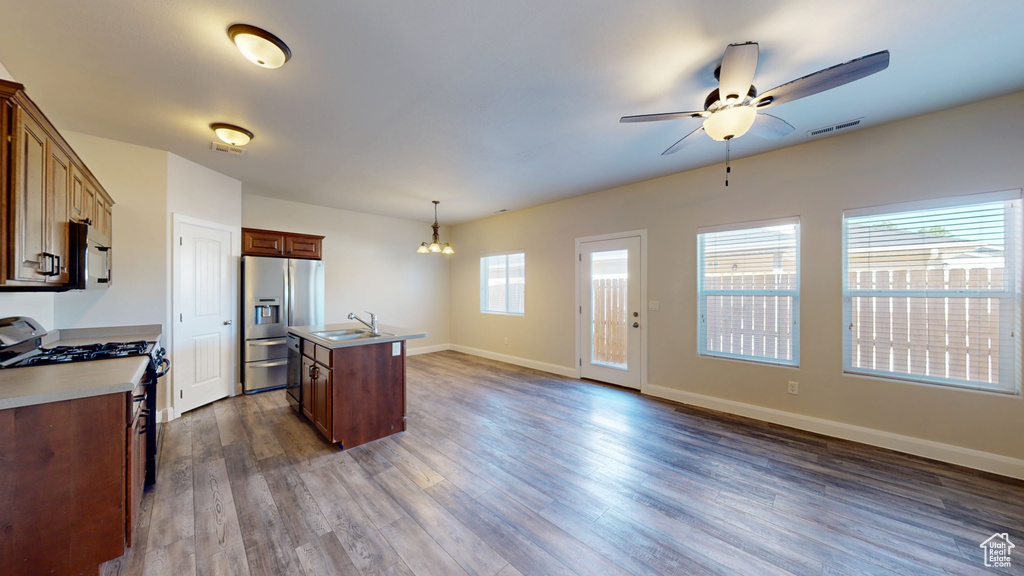 Kitchen with stainless steel refrigerator with ice dispenser, gas range oven, a chandelier, ceiling fan, and an island with sink