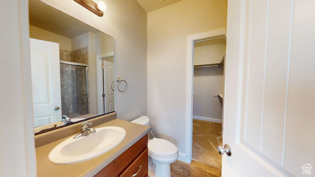 Bathroom with an enclosed shower, vanity, toilet, a spacious closet, and wood finished floors