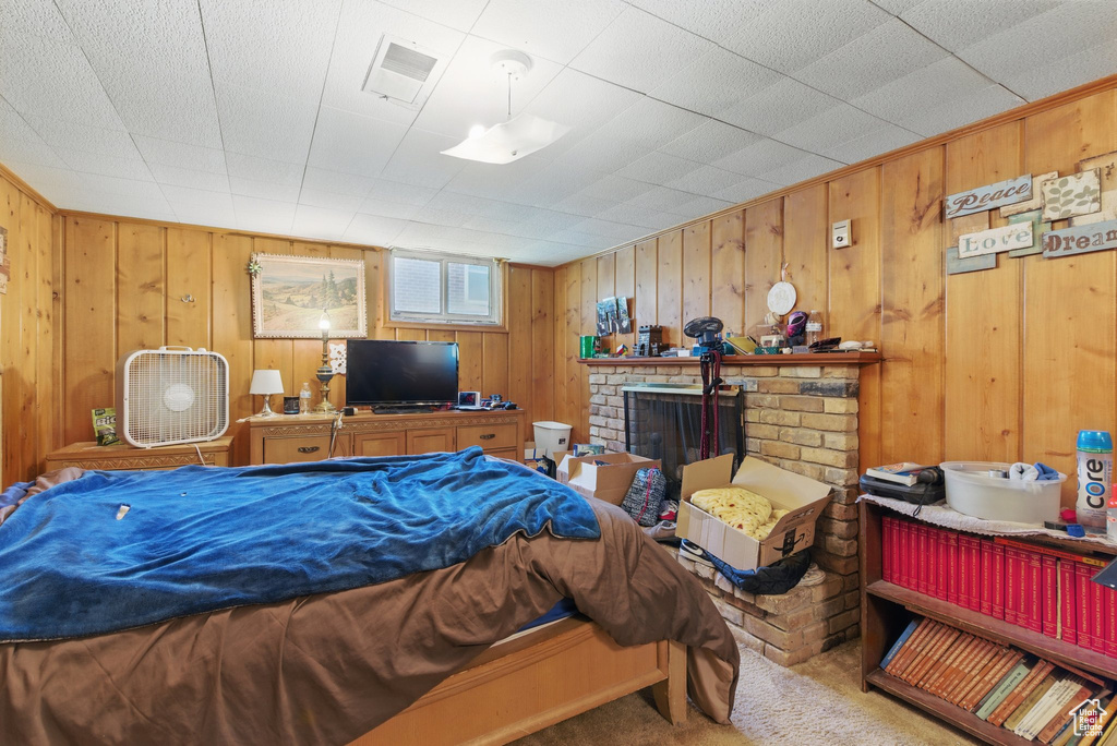 Bedroom featuring carpet floors, wooden walls, and a brick fireplace