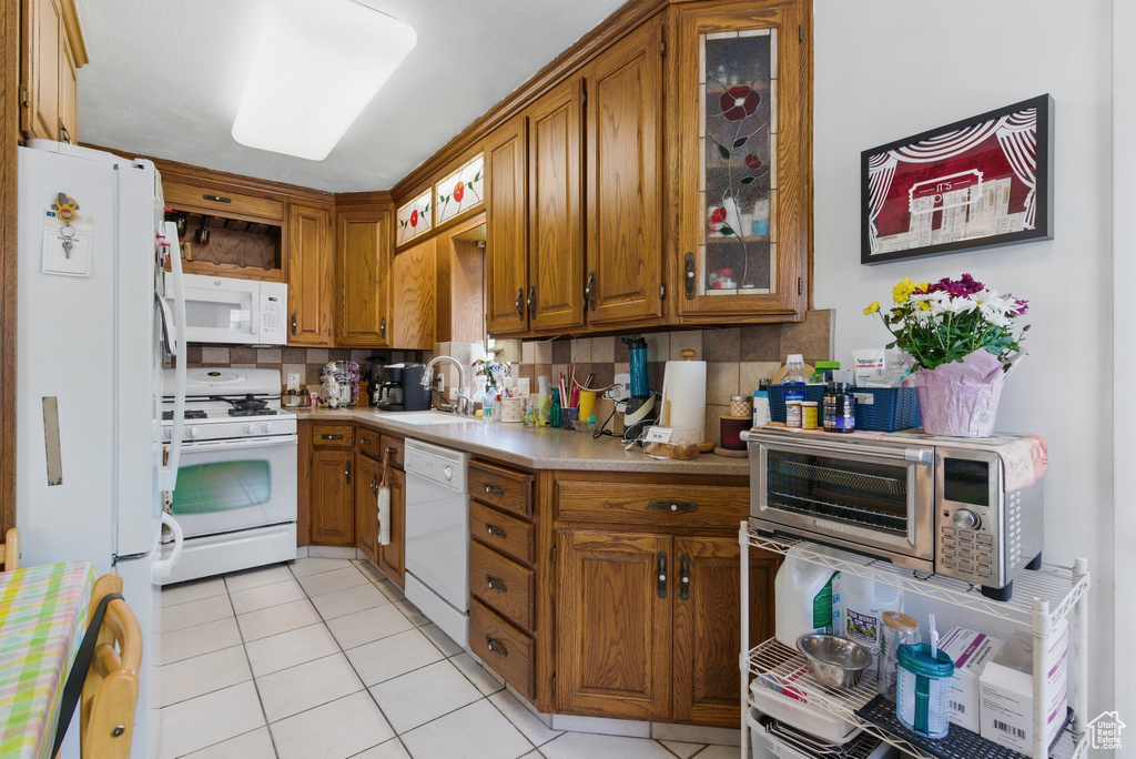 Kitchen featuring white appliances, a sink, brown cabinetry, light countertops, and backsplash