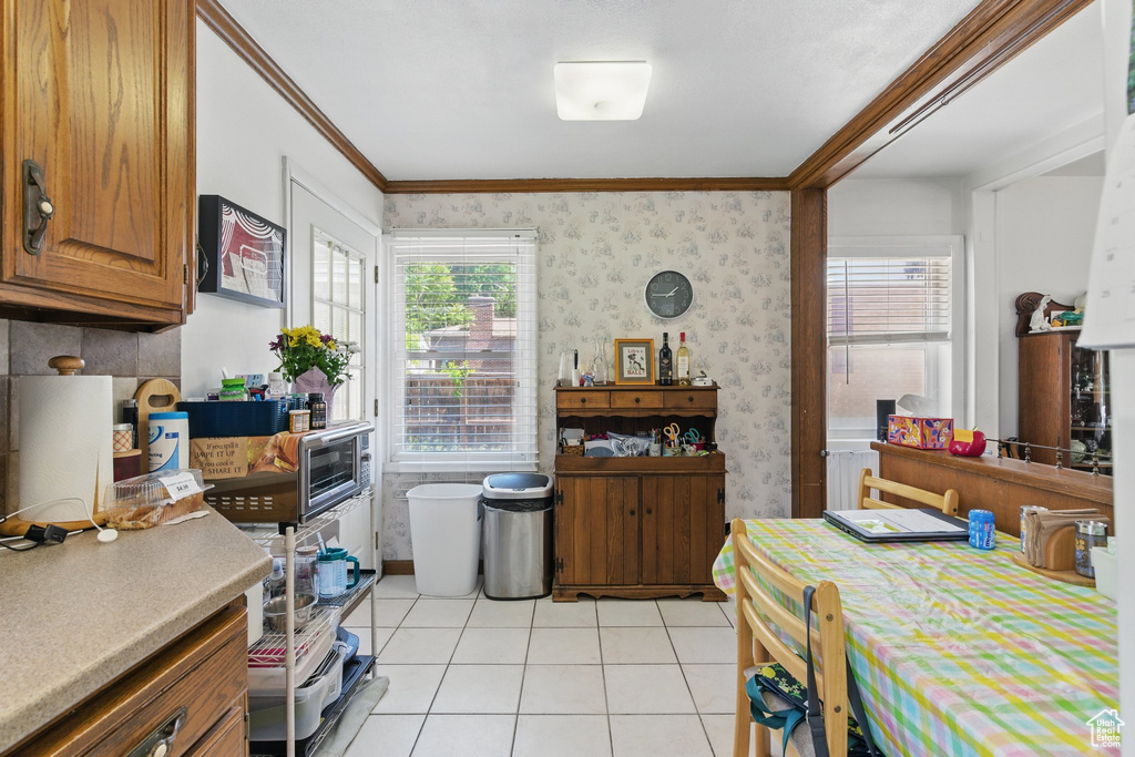 Dining space with light tile patterned flooring, wallpapered walls, plenty of natural light, and ornamental molding