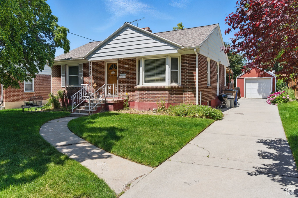 Bungalow-style home with brick siding, an outbuilding, a detached garage, driveway, and a front yard