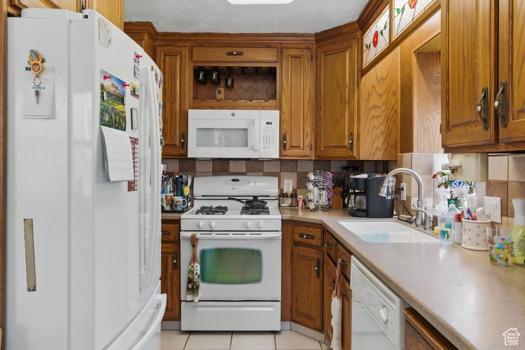 Kitchen with white appliances, a sink, light countertops, and tasteful backsplash