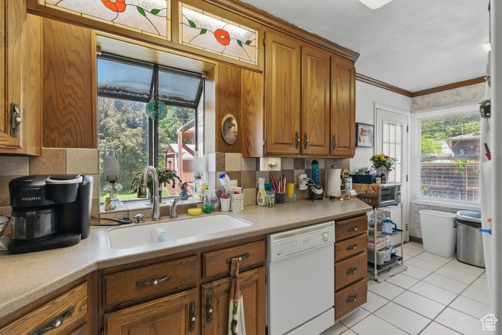 Kitchen with dishwasher, a sink, brown cabinetry, decorative backsplash, and crown molding