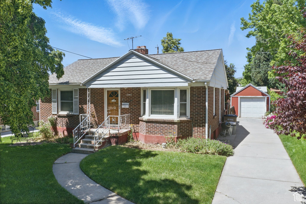Bungalow featuring roof with shingles, brick siding, an outdoor structure, a chimney, and a front yard