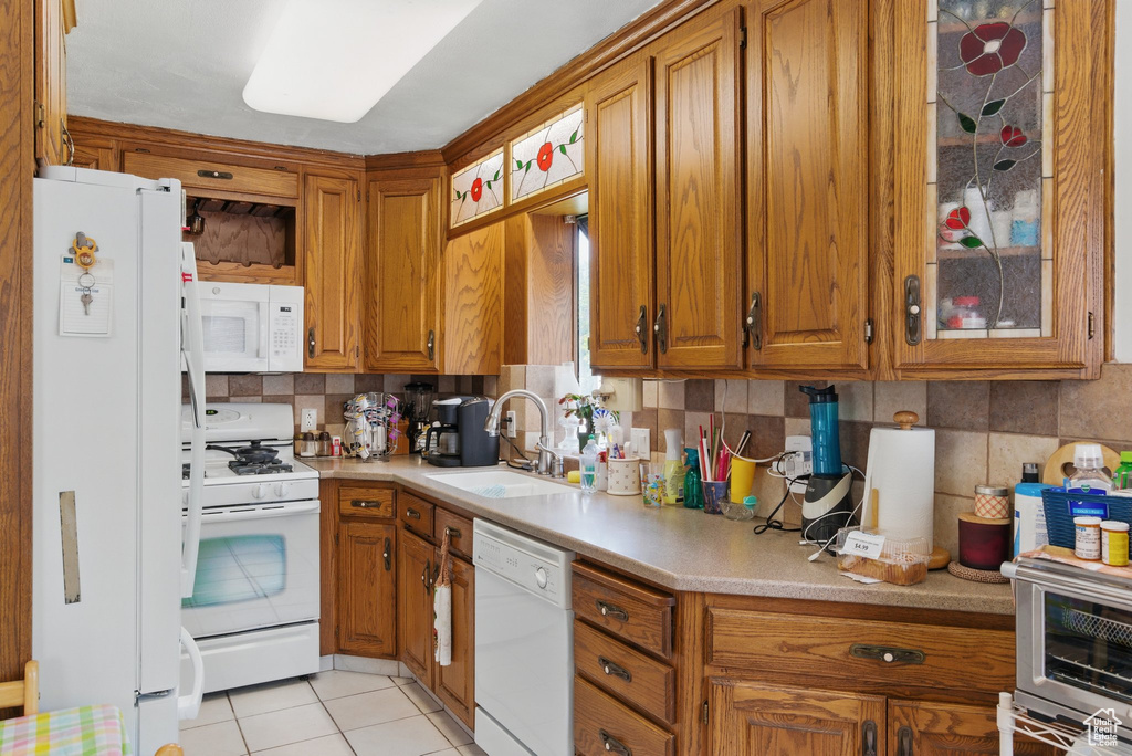 Kitchen with white appliances, a sink, brown cabinets, and light countertops
