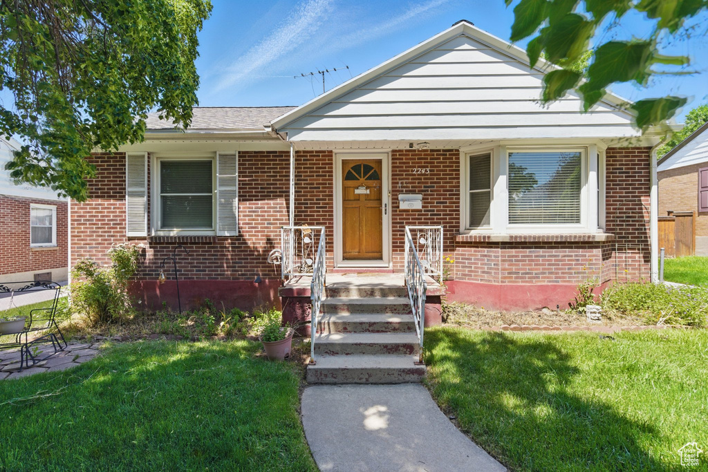 Bungalow with brick siding, a front lawn, and roof with shingles