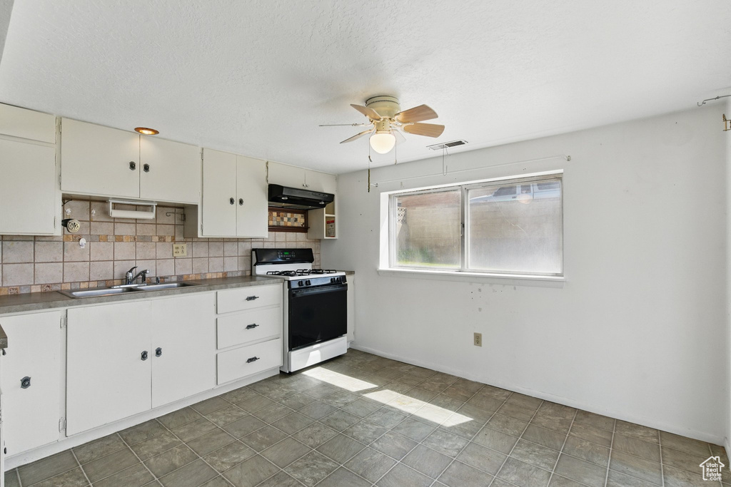 Kitchen featuring white gas stove, under cabinet range hood, a sink, a ceiling fan, and decorative backsplash