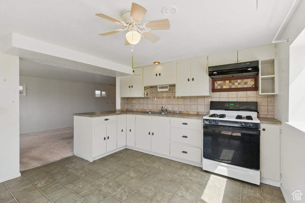Kitchen featuring gas range gas stove, under cabinet range hood, a sink, a ceiling fan, and backsplash