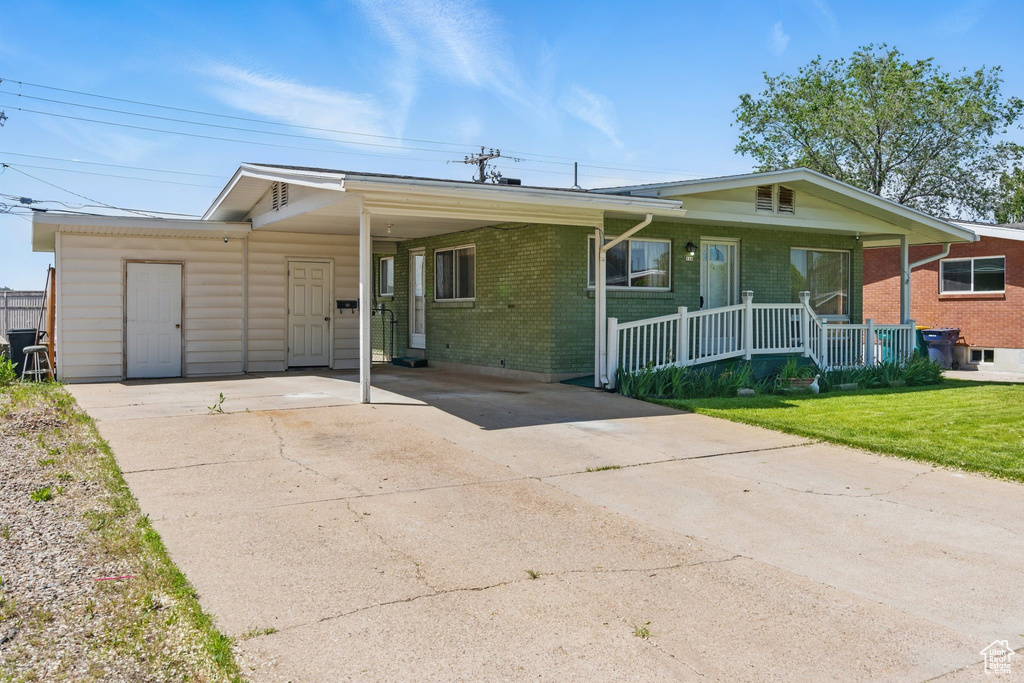 Ranch-style home featuring concrete driveway, a porch, brick siding, a front yard, and an attached carport
