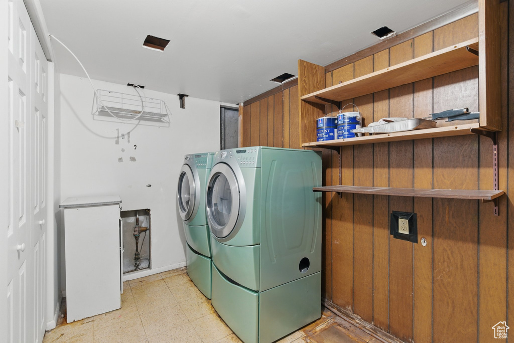 Washroom featuring washing machine and dryer, wooden walls, and light floors