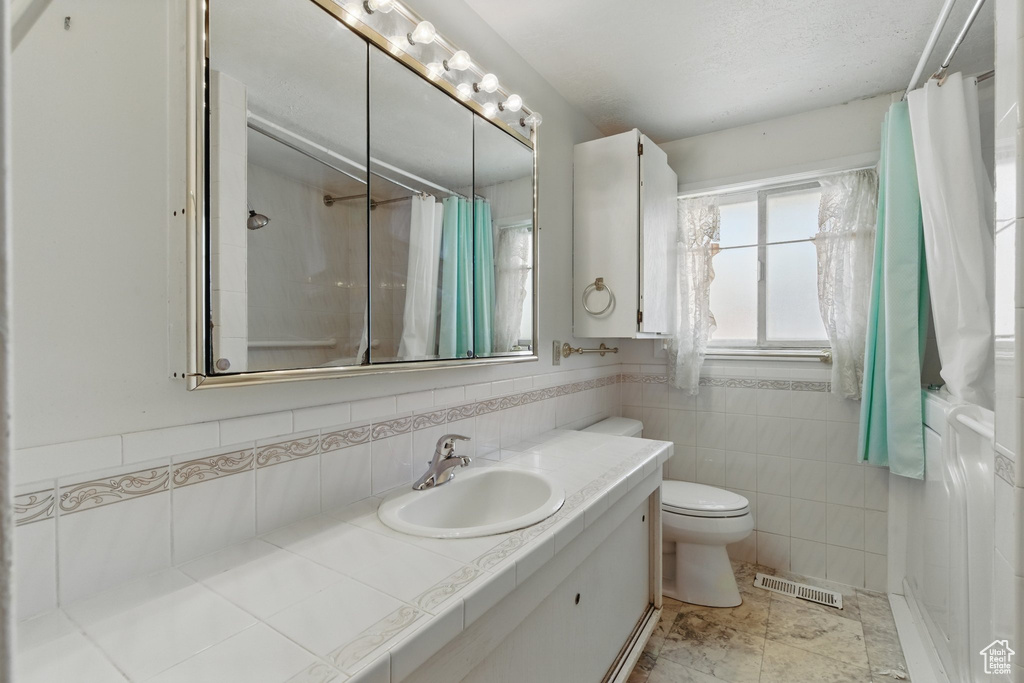 Bathroom with vanity, toilet, a shower with curtain, and tile walls