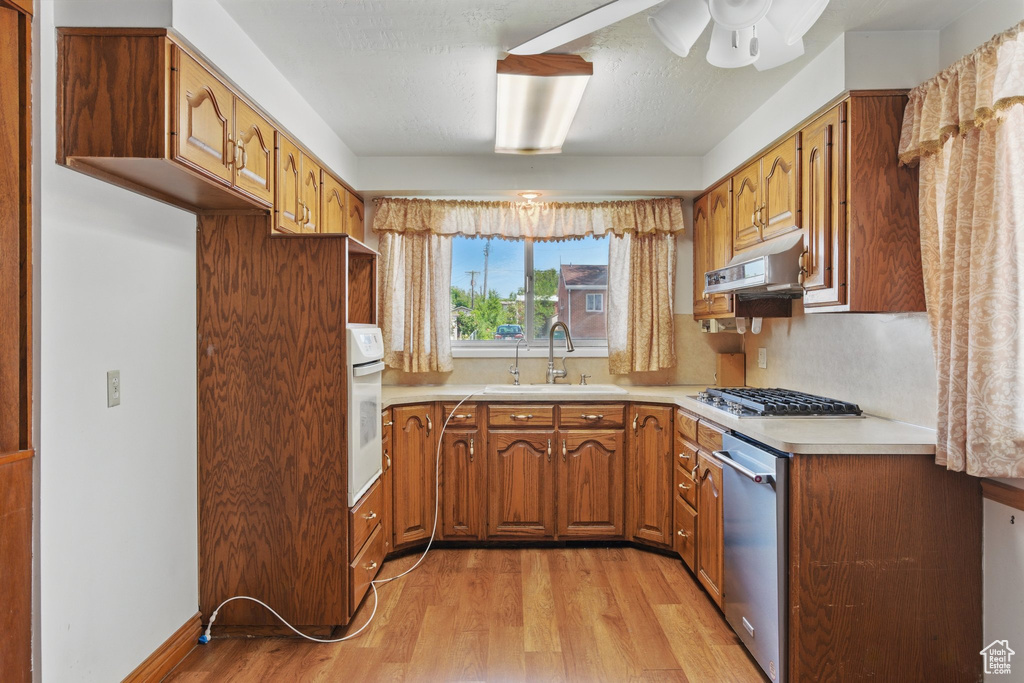 Kitchen with a sink, light wood-style flooring, stainless steel appliances, brown cabinets, and light countertops