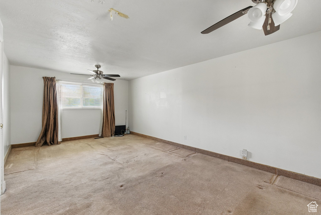 Spare room with a ceiling fan, light carpet, and baseboards