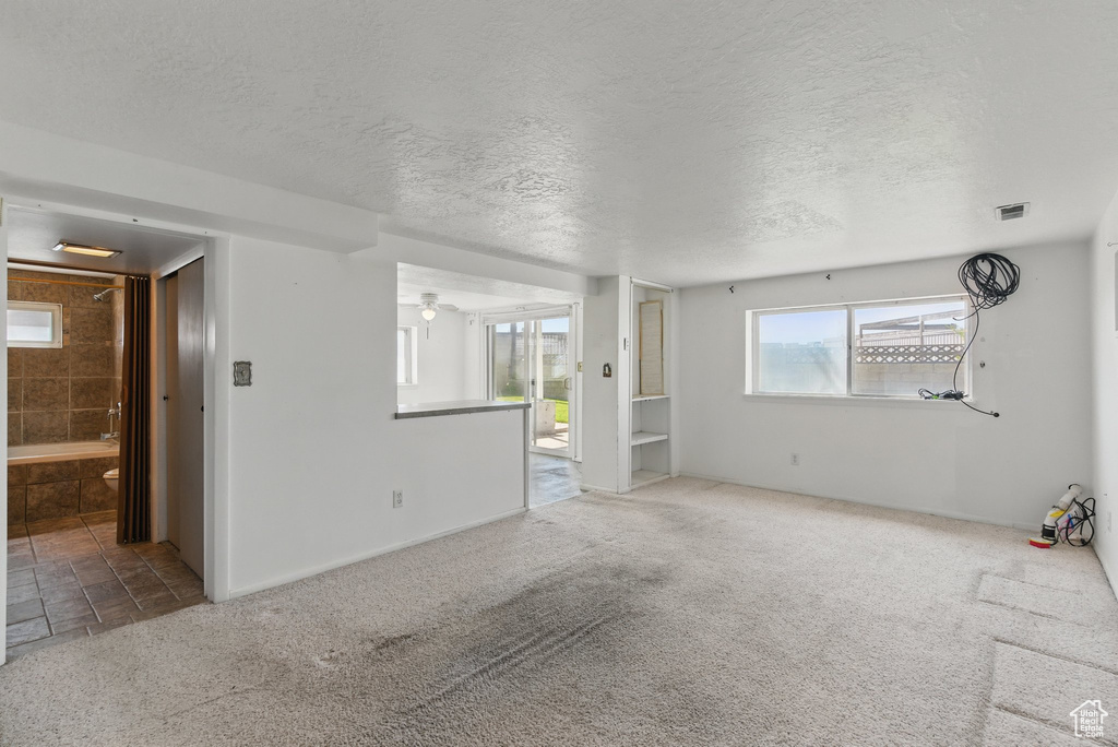 Carpeted spare room with healthy amount of natural light, a textured ceiling, ceiling fan, and baseboards