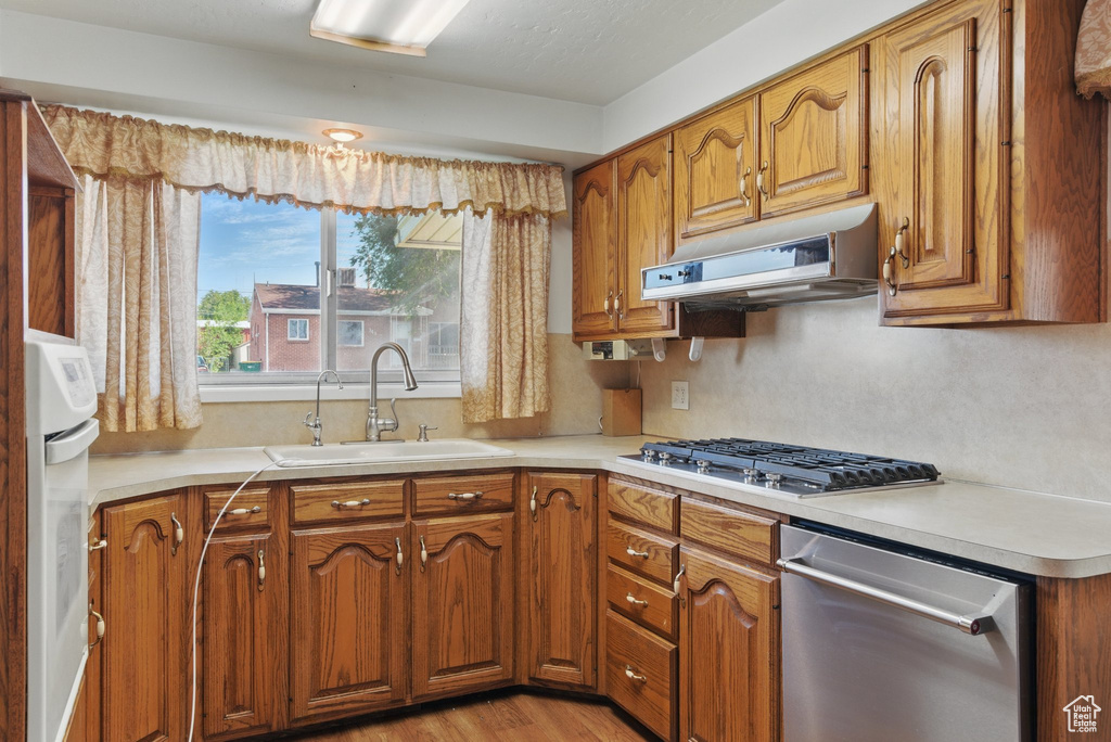 Kitchen featuring a sink, stainless steel appliances, under cabinet range hood, and brown cabinets