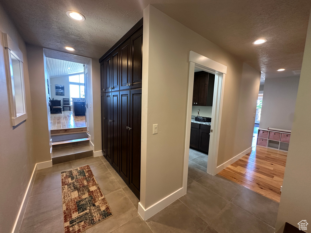 Hall featuring a textured ceiling, baseboards, recessed lighting, and light tile patterned floors