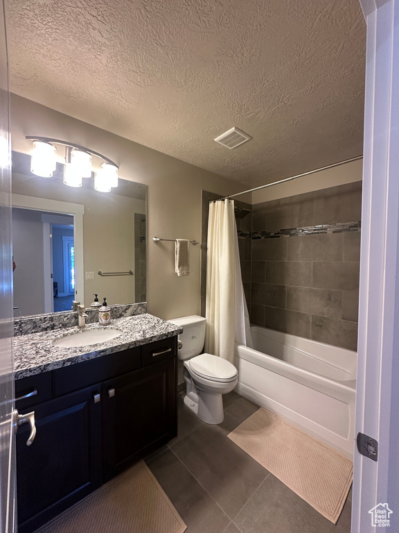 Bathroom featuring vanity, toilet, shower / bath combination with curtain, tile patterned flooring, and a textured ceiling