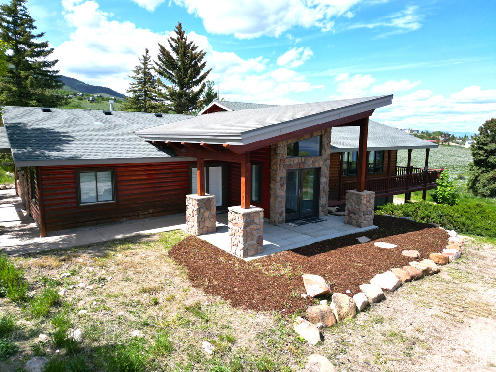 View of front of home with roof with shingles, a patio area, stone siding, and a mountain view