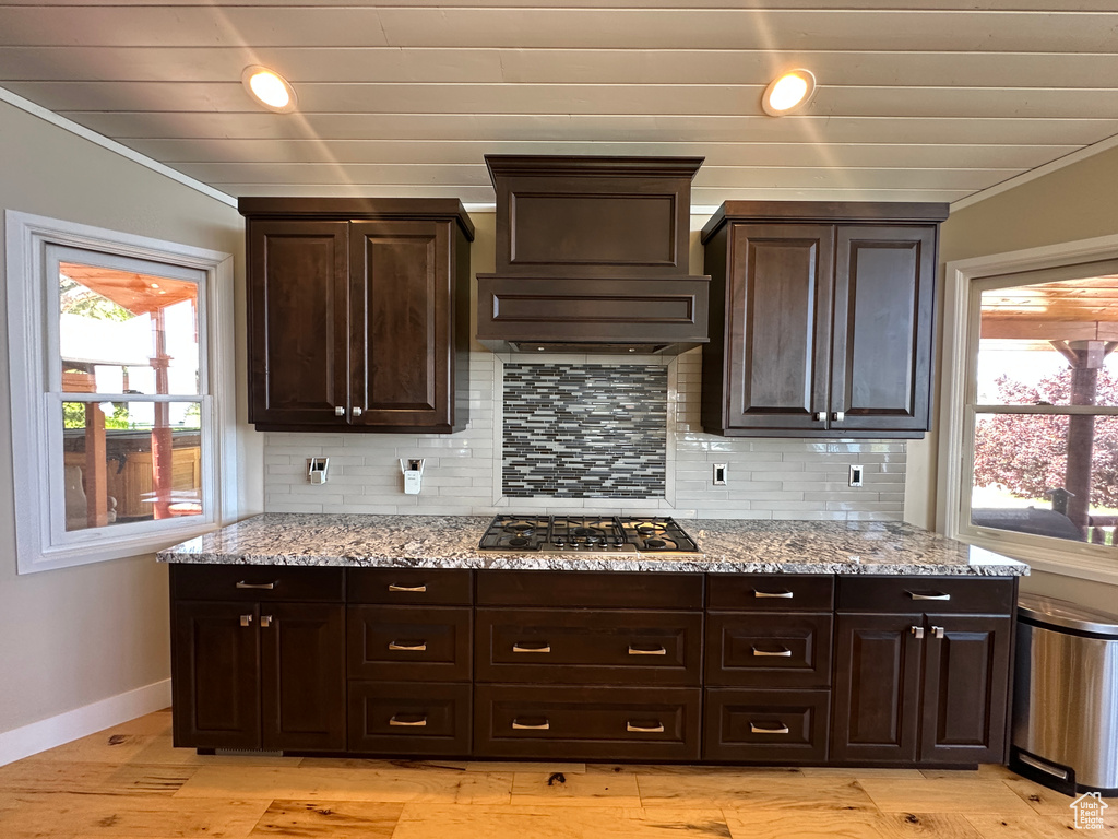 Kitchen with light stone countertops, crown molding, dark brown cabinetry, baseboards, and tasteful backsplash